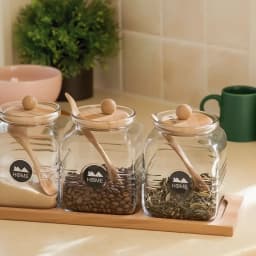 Three clear square glass storage jars with light brown bamboo lids, matching spoons, and a bamboo tray on white background - view 4