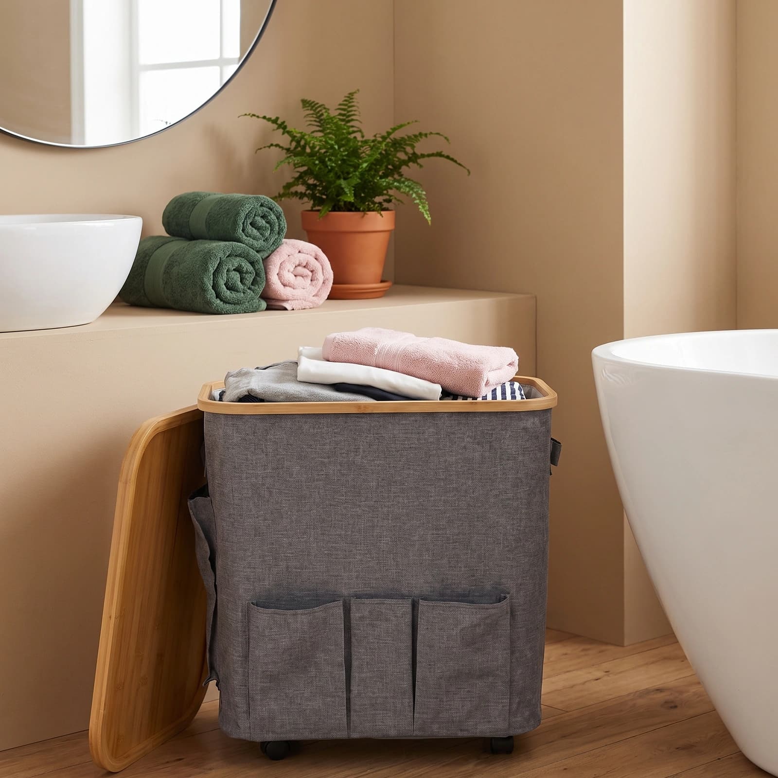 Grey fabric storage hamper with a light brown bamboo wood lid and three front pockets, on wheels.