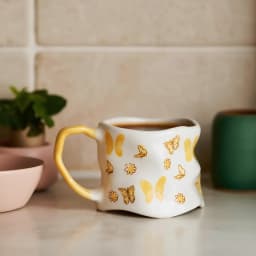 Off-white ceramic mug with a yellow handle and yellow butterfly and flower designs, on a white background - view 6