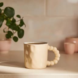 Light yellow ceramic mug with a textured body and a unique bubble-shaped handle, isolated on a white background. - view 1