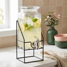 Clear rectangular glass beverage dispenser with an embossed design, silver spigot, and black metal stand on a white backgrou… - view 1