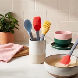Three silicone kitchen utensils with grey handles and colorful heads: a blue spoon, a red spatula, and a yellow basting brus… - view 1
