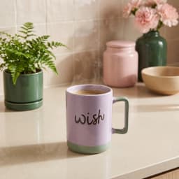 كوب سيراميك بنفسجي فاتح بيد وقاعدة خضراء، مكتوب عليه كلمة "wish" بالأسود. - view 1