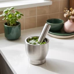 Silver brushed stainless steel mortar and pestle set with a clear plastic lid, filled with spices, on a light kitchen counte… - view 3