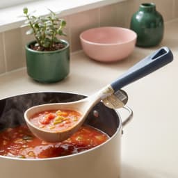 Beige silicone ladle with a dark blue handle, featuring a hanging hole, on a white background. - view 1
