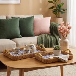 Two rectangular woven khous serving trays with blue floral plastic liners and wooden bead handles on a wooden coffee table. - view 1