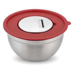 Stainless steel mixing bowl with red whisk and red lid on a light kitchen counter, next to a pink potted plant. - view 3
