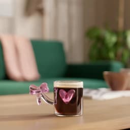 Single clear glass mug with a pink bow-shaped handle and a pink heart decoration on the side, on a white background. - view 3