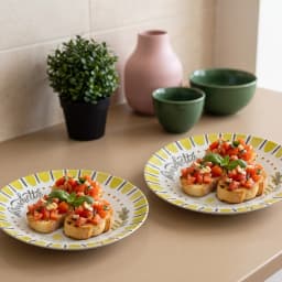 Two round white porcelain plates with a yellow-green border, olive oil bottle, olive branches, and 'bruschetta' design. - view 1