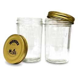 Four clear glass cylindrical storage jars with gold metal lids on a kitchen counter, filled with jam, pasta, and spices. - view 7