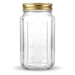 Four clear glass cylindrical storage jars with gold metal lids on a kitchen counter, filled with jam, pasta, and spices. - view 4