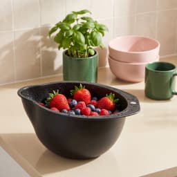 Black plastic rice washing and straining bowl with small holes, filled with strawberries, blueberries, and raspberries on a… - view 1