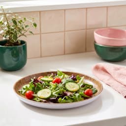Round melamine plate with brown wood grain interior and white rim, holding a fresh salad on a white kitchen counter. - view 1
