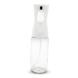 Clear glass oil spray bottle with a white fine mist top, filled with olive oil, standing on a light kitchen counter. - view 2