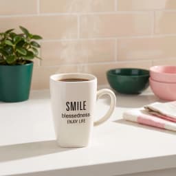 Single white ceramic mug with a slightly squared top and 'SMILE blessedness ENJOY LIFE' text, on a white shelf. - view 1