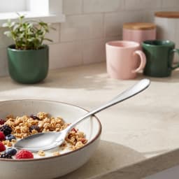 Single silver stainless steel eating spoon with a polished finish, lying diagonally on a white background. - view 1