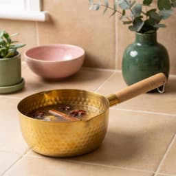 Golden hammered stainless steel milk pan with a light wooden handle, containing a clear liquid with star anise and cinnamon… - view 1