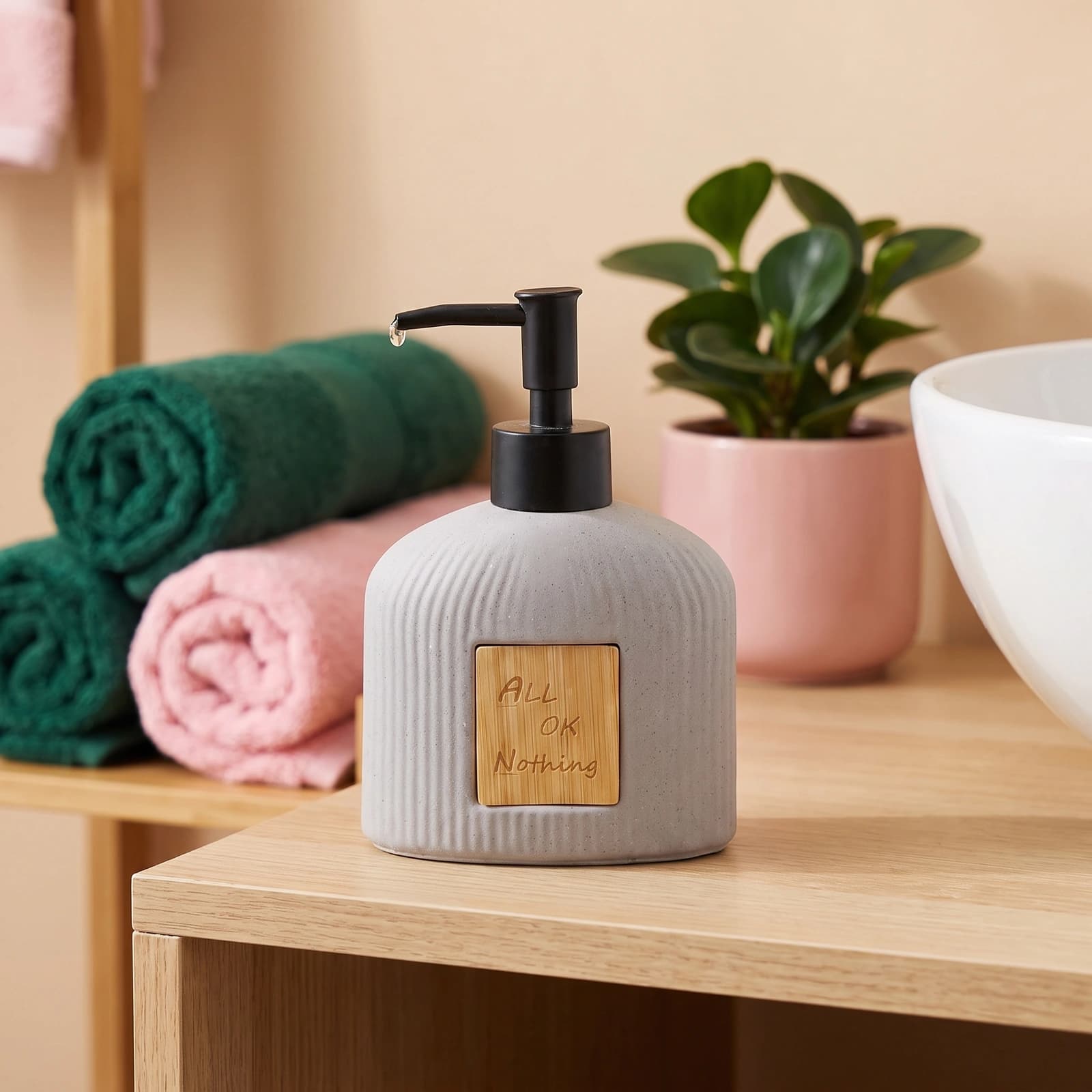 Grey speckled ceramic soap dispenser with a black pump and a light wooden label engraved with 'ALL OK Nothing' on a white ba…