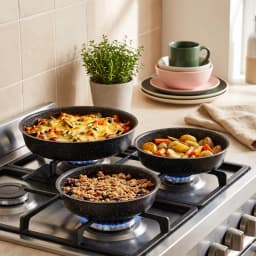 Set of three round black speckled granite baking dishes, stacked from largest to smallest, on a white surface. - view 1