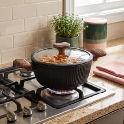 Black ceramic casserole pot with ribbed texture, glass lid, and wood-look ceramic handles, shown in its packaging. - view 1