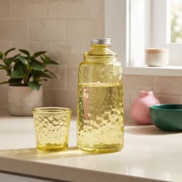 Light green textured glass bottle with silver cap and matching small glass cup on a white shelf. - view 1