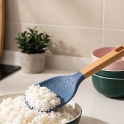 A single blue silicone rice paddle with a light brown wooden handle, resting on a clean white shelf. - view 1