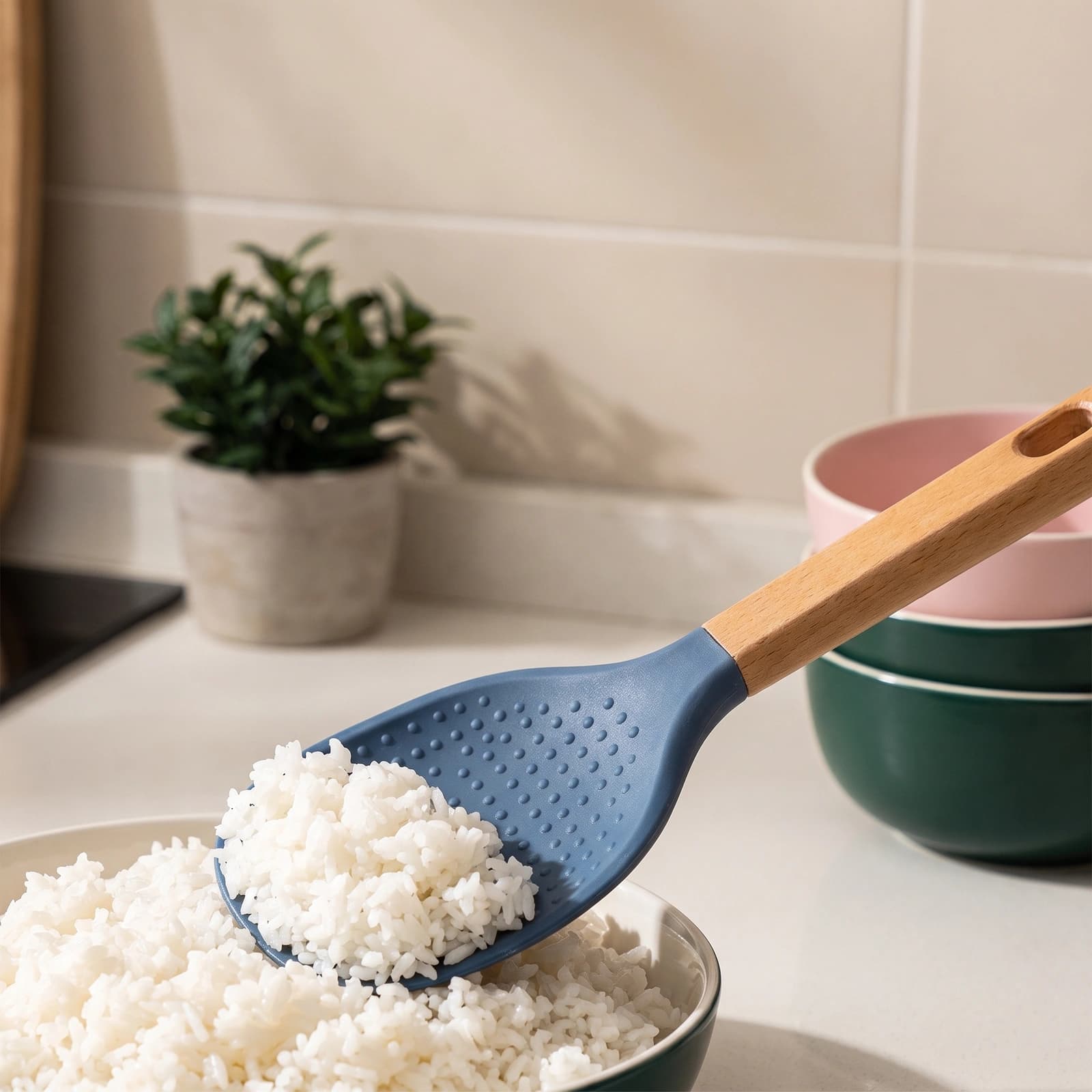 A single blue silicone rice paddle with a light brown wooden handle, resting on a clean white shelf.