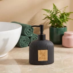 Black speckled ceramic soap dispenser with vertical ridges and a black pump, featuring a small wooden label. - view 1