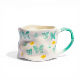 Off-white ceramic mug with a yellow handle and yellow butterfly and flower designs, on a white background - view 3
