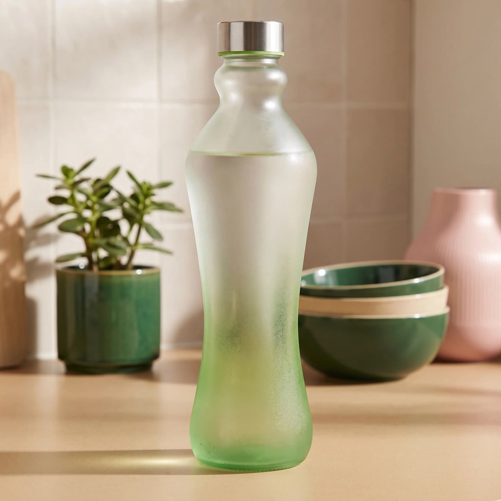 Tall frosted glass bottle with a green gradient bottom and a silver screw cap on a white background