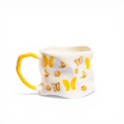 Off-white ceramic mug with a yellow handle and yellow butterfly and flower designs, on a white background - view 2