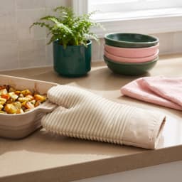 Single beige and light pink silicone and fabric oven mitt with a ribbed palm, resting in a white styrofoam tray. - view 3