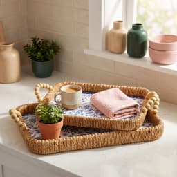 Two rectangular woven khous serving trays with blue floral plastic liners and wooden bead handles on a wooden coffee table. - view 5