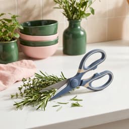 One pair of dark blue and cream silicone handle kitchen shears with serrated edge on a white shelf. - view 4