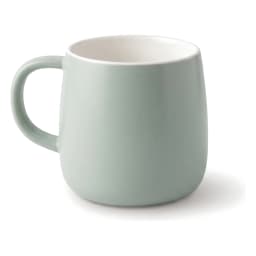 Single light green ceramic mug with a white interior, sitting on a white shelf against a light brown wooden background. - view 2