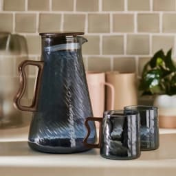Blue textured glass pitcher with brown lid and handle, alongside one matching glass and one mug, filled with cold beverage. - view 5