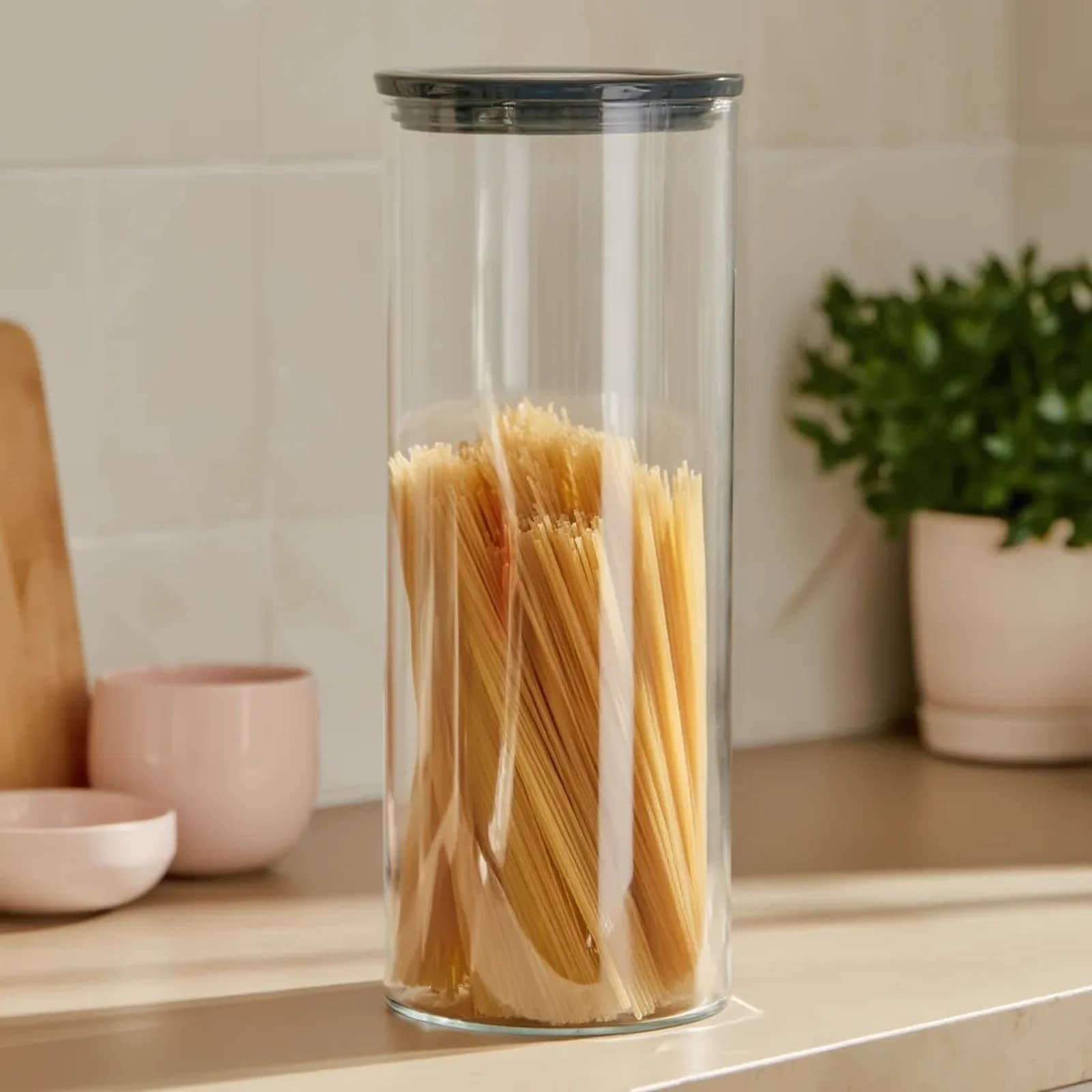 Tall, clear cylindrical glass storage jar with a dark grey flat lid on a pure white background