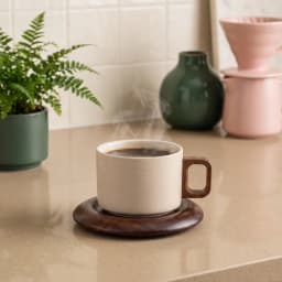 Beige speckled ceramic mug with dark wood handle on a round dark wood saucer, isolated on a white background. - view 1