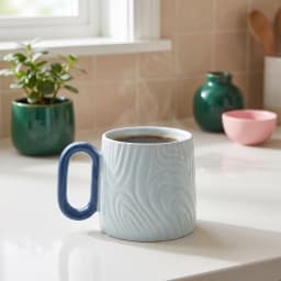 Light blue ceramic mug with a subtle swirl pattern and a dark blue handle, on a white surface with a wooden background. - view 1