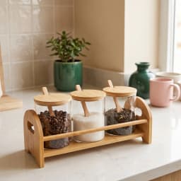 Set of 3 clear glass storage jars with natural wood lids and spoons on a matching wood stand, on a kitchen counter. - view 1
