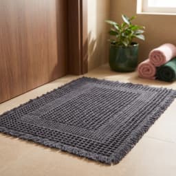 Rectangular grey waffle weave cotton bath mat with fringed edges, viewed from above on a white background. - view 1