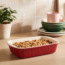 Single rectangular red porcelain loaf pan with ribbed exterior and cream interior on a white shelf - view 1