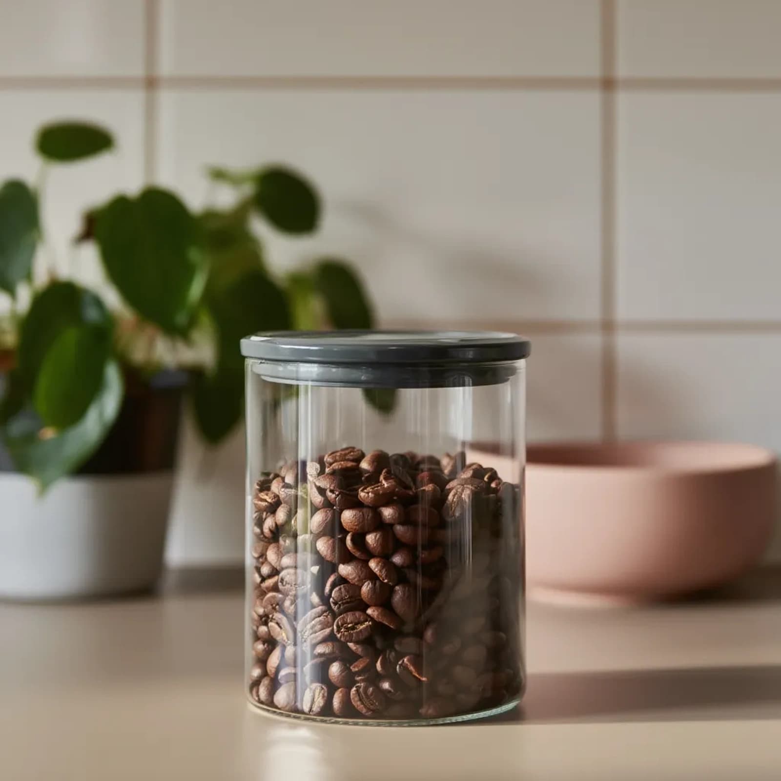 Clear cylindrical glass storage jar with a dark grey plastic lid and a visible seal, on a white background.