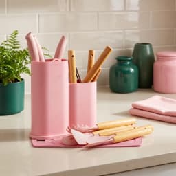 Pink kitchen utensil set with wooden handles in a pink holder, including spatulas, spoons, and tongs on a white background. - view 1