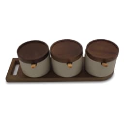 Three cream porcelain spice jars with wooden lids and spoons on a wooden tray, filled with spices, on a kitchen counter. - view 2
