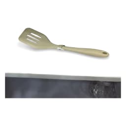 A single beige silicone slotted spatula with a hanging hole, lying diagonally on a white background. - view 2
