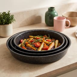 Set of three round black speckled granite baking dishes, stacked from largest to smallest, on a white surface. - view 5