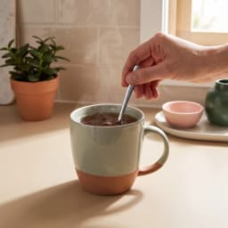 Single ceramic mug with a light green top and a terracotta bottom, on a white shelf. - view 3