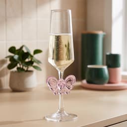 Clear glass champagne flute with a slender stem and base, featuring a translucent pink butterfly decoration on the stem. - view 1
