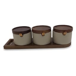 Three cream porcelain spice jars with wooden lids and spoons on a wooden tray, filled with spices, on a kitchen counter. - view 3
